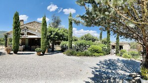 A rustic stone building with a gravel driveway, surrounded by tall cypress trees and a vineyard in the background. - Bastides w/Pools A/C sleeps 12 guests on vineyards walking distance to village   (Le Plan-de-la-Tour)