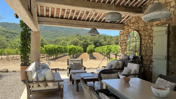 An outdoor patio with a stone wall, wicker furniture, and a view of vineyards. - Bastides w/Pools A/C sleeps 12 guests on vineyards walking distance to village   (Le Plan-de-la-Tour)