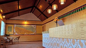 A room with a high ceiling, wooden beams, patterned wallpaper, a map on the wall, and wicker furniture. - Hotel Spiti Villa Himalayan Brothers (Spiti)