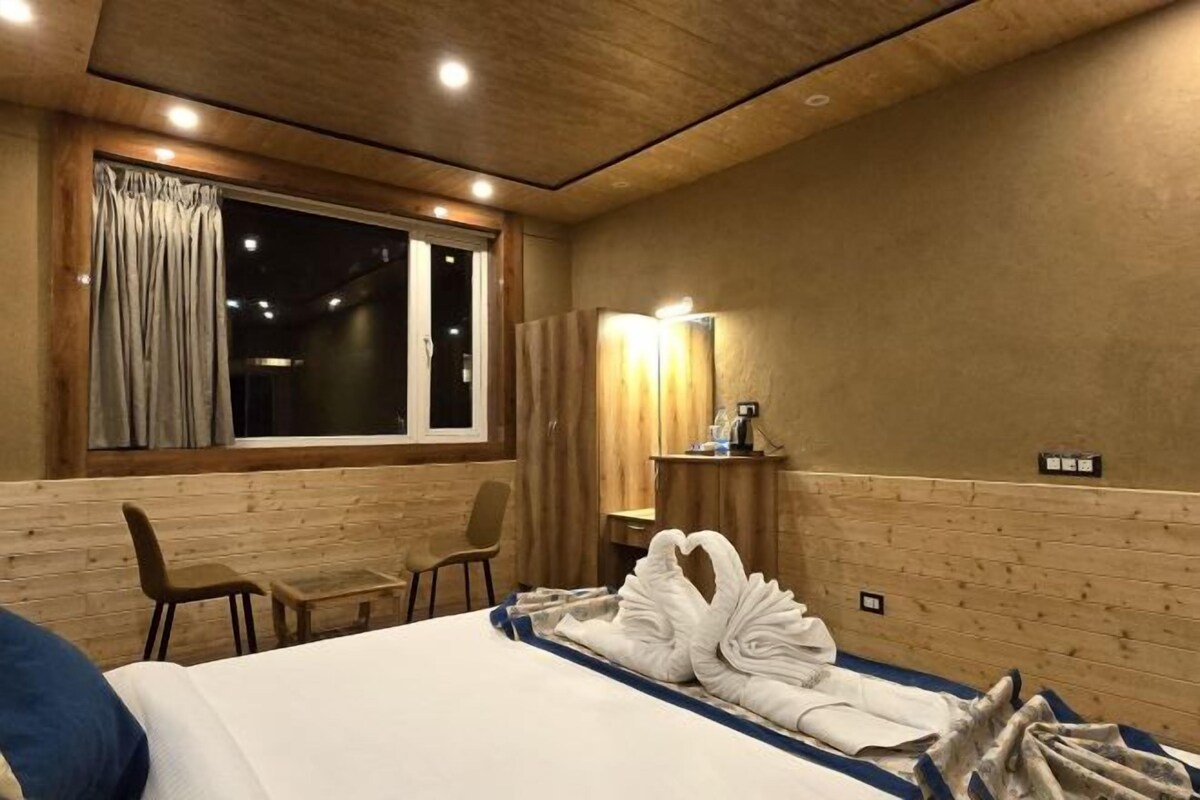 A hotel room with a bed, a desk, a chair, a window with curtains, and a wall-mounted mirror.