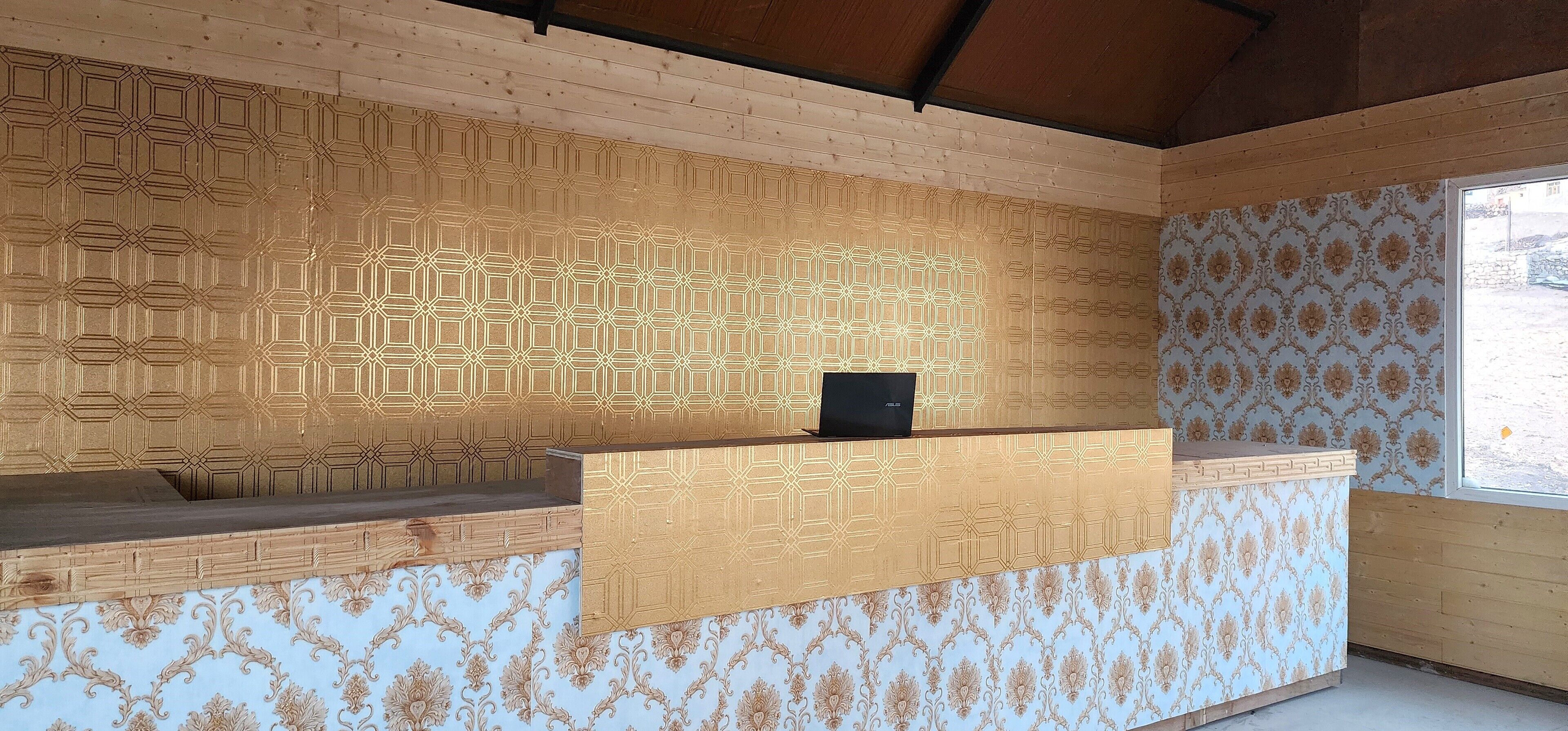 A room with a wooden ceiling, a patterned wall, a reception desk, and a window with a view.