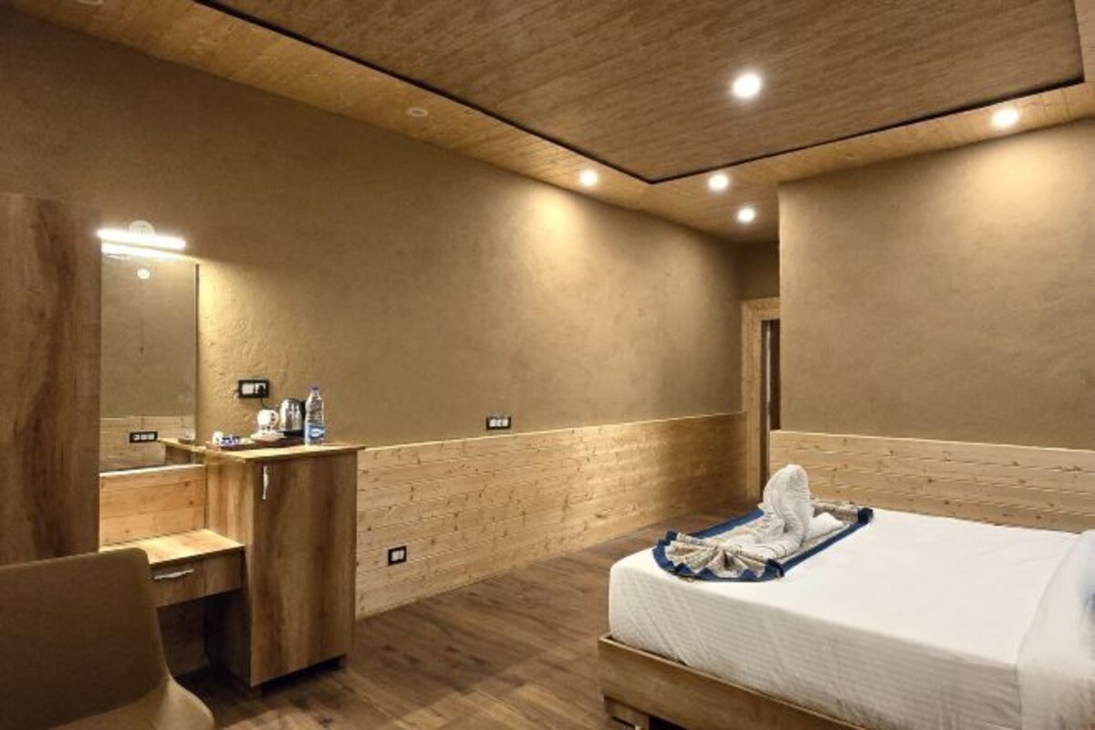 A hotel room with a wooden bed, a wooden desk, a mirror, and a small bathroom area.