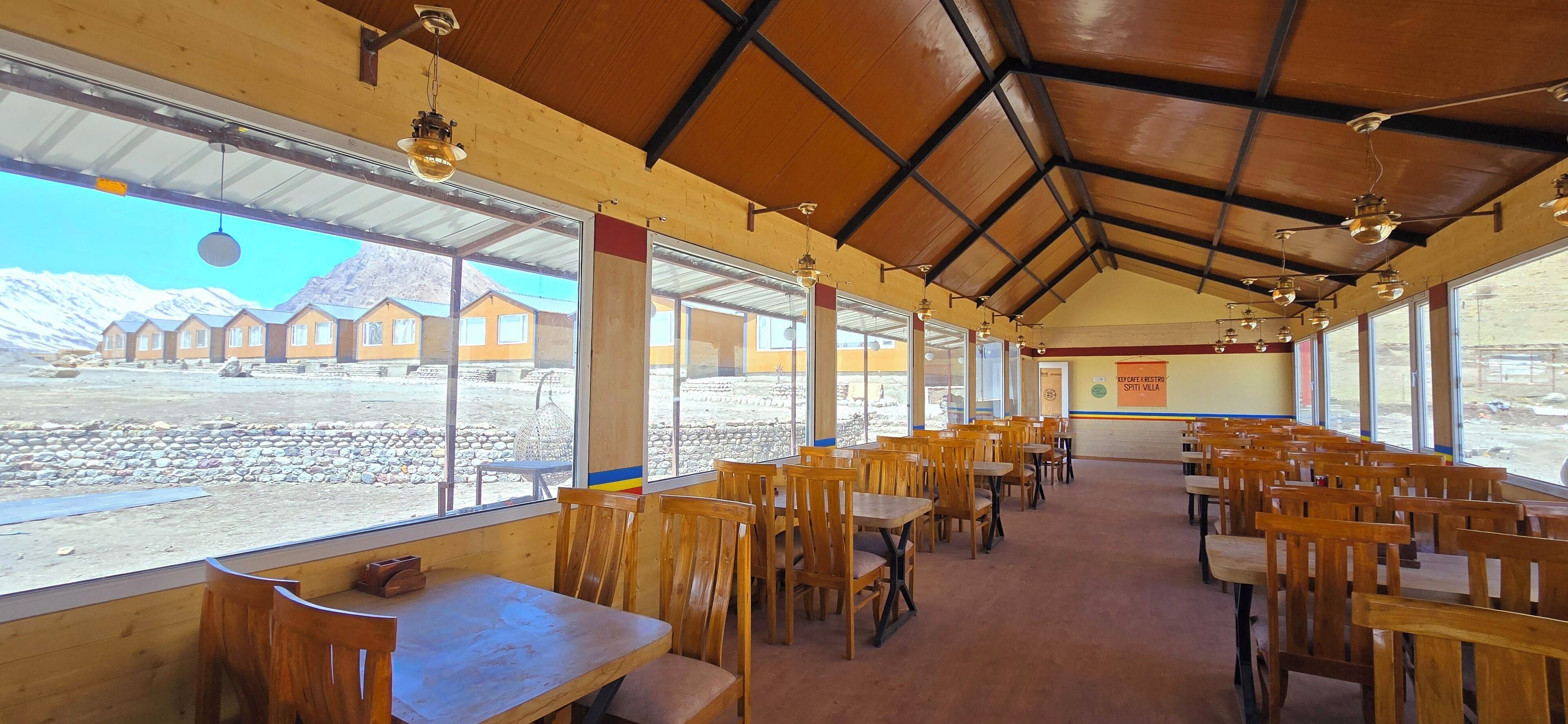 A restaurant with wooden tables and chairs, large windows, and a view of snow-covered houses.