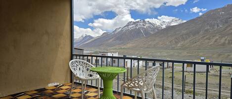 Un balcón con vistas a montañas nevadas, un suelo a cuadros y dos sillas blancas.