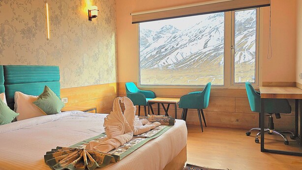 A hotel room with a large bed, a desk, two chairs, and a view of a snowy landscape through a large window. - Hotel Spiti Villa Himalayan Brothers (Spiti)