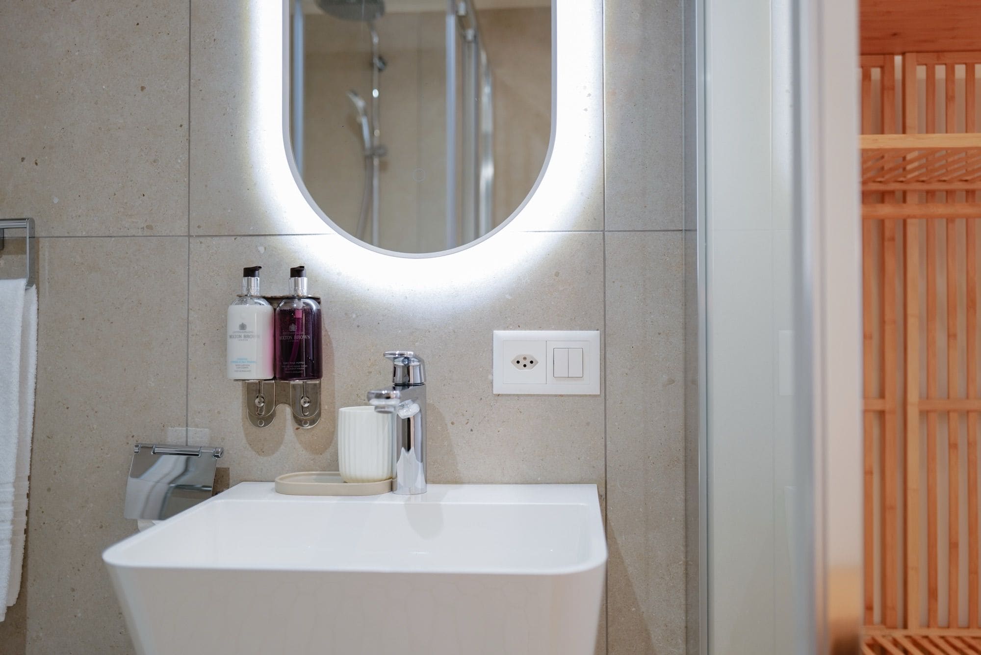 Un baño con un lavamanos blanco, dos botellas de loción, un espejo y un cabezal de ducha.