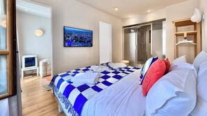 Ein Schlafzimmer mit kariertem Bettbezug, einem an der Wand befestigten Fernseher, einem Kleiderschrank und einem Spiegel.