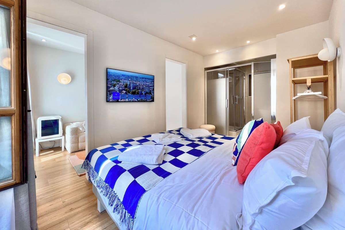 A bedroom with a checkered bedspread, a television on the wall, a wardrobe, and a mirror.