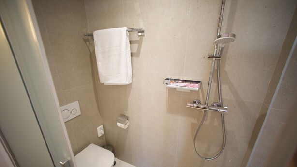 Une petite salle de bain moderne équipée de toilettes, d’une douche et d’un porte-serviettes.