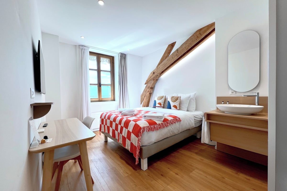 A modern bedroom with a bed, bedside table, and a bathroom with a sink and mirror.