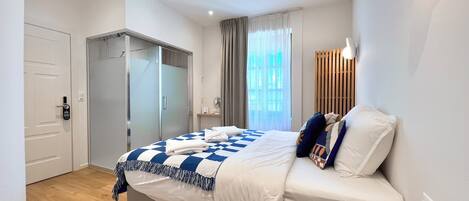 Ein modernes Hotelzimmer mit Bett, Schrank, Badezimmer und einem Fenster mit Vorhängen.