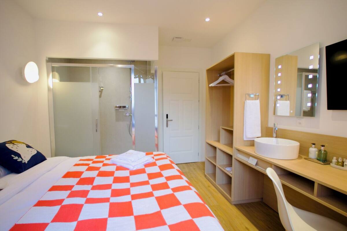 A hotel room with a bed, a desk, a mirror, and a wardrobe.