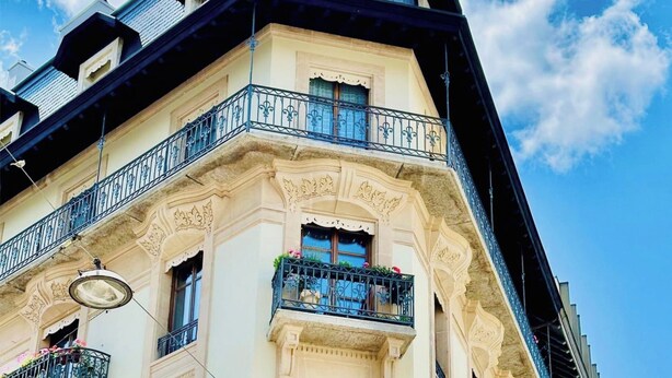 Ein Eckgebäude mit aufwendigen architektonischen Details, darunter ein Balkon mit schmiedeeisernen Geländern und Blumenkästen.