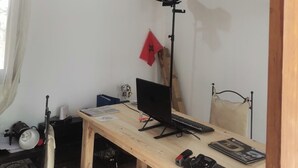 Una habitación con un escritorio de madera, una computadora, una silla, una araña y un aire acondicionado, además de una bandera roja en la pared.