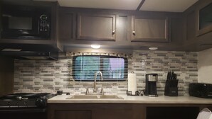 Une cuisine équipée d’un four à micro-ondes, d’une cuisinière, d’un évier et d’une fenêtre avec des stores.