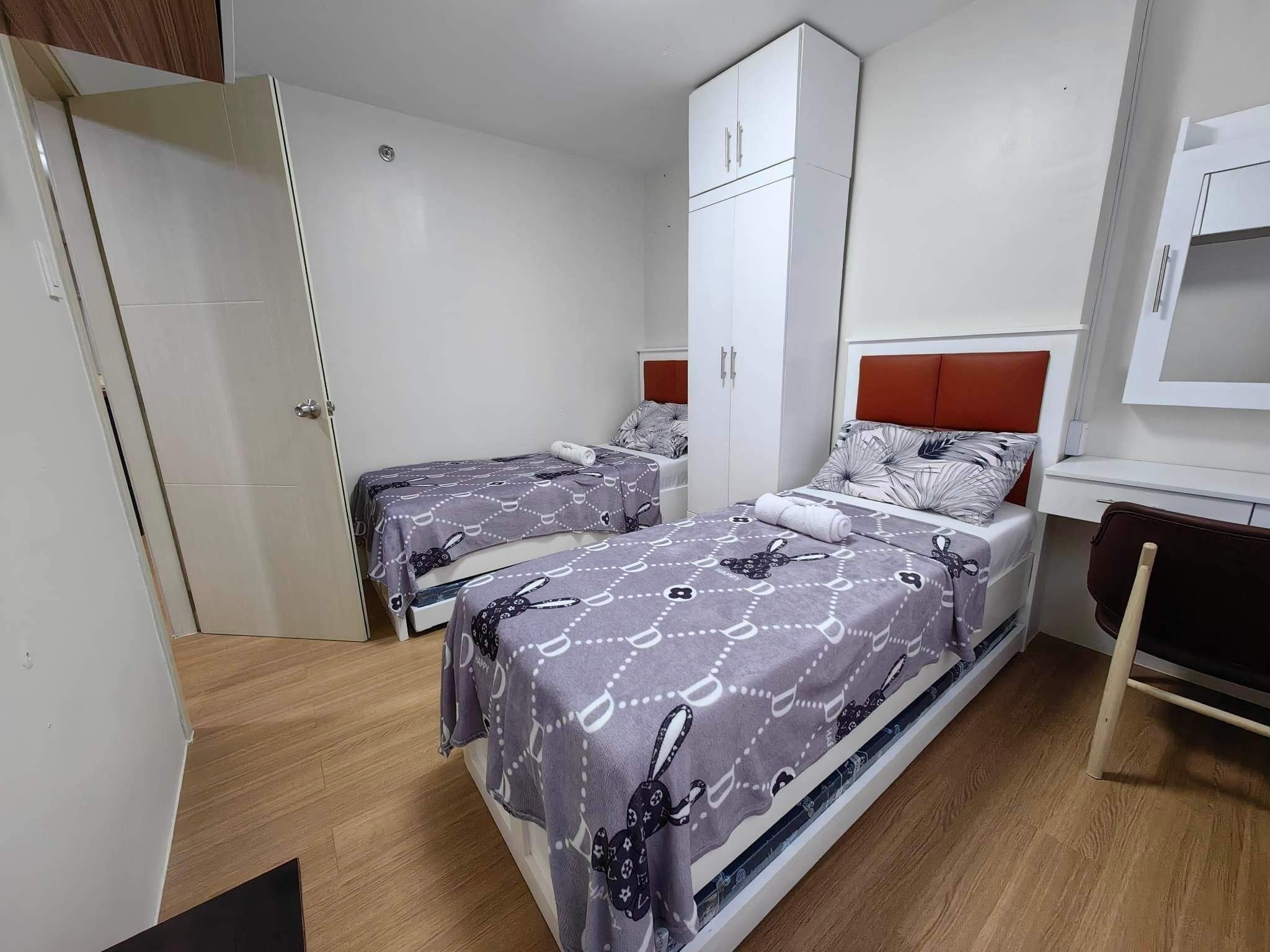 A bedroom with two beds, a wardrobe, and a desk.