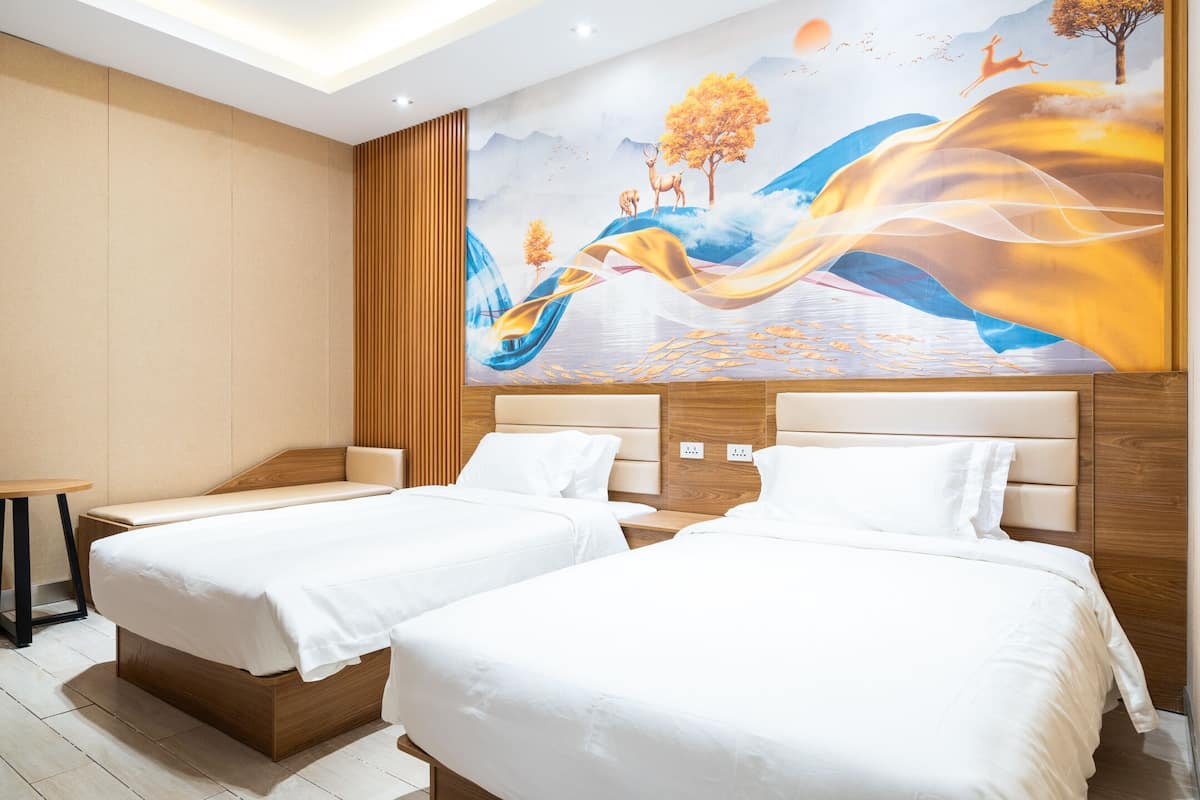 A hotel room with two beds, a wooden headboard, a mural on the wall, and a small table.