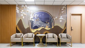 A reception area with two beige armchairs, a round table, and a decorative wall with a traditional painting and hanging flowers. - Home me Hotel (Makati)