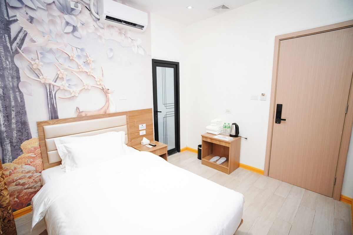 Quarto de hotel com cama, mesa de cabeceira, guarda-roupa e um mural na parede.