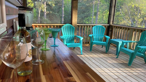 Une terrasse en bois avec des chaises turquoise et une table sur laquelle sont disposés des verres à vin et des bouteilles.