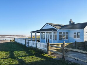Uma casa costeira com varanda coberta, quintal cercado e vista para o mar.