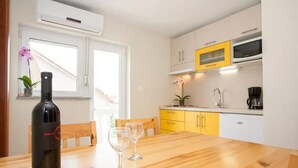 A kitchen with a wooden table, two wine glasses, a bottle of wine, a microwave, and yellow cabinets. - Two bedroom apartment for 3 person (Jadranovo)
