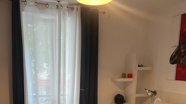 A bedroom with a bed, a nightstand, a lamp, a window with curtains, and a wall-mounted shelf. - Montmartre-appartement Climatisé -3min Sacré-cœur (Paris)