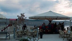 An outdoor seating area with tables and chairs, a large umbrella, and a playground with a slide.