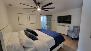 A bedroom with a bed, a ceiling fan, a TV, a dresser, and a chair.