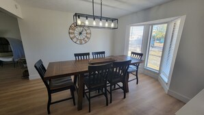 A dining area with a wooden table and chairs, a wall clock, and a ceiling light fixture.