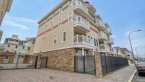 A multi-story residential building with balconies, a stone base, and a paved sidewalk.