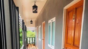 A corridor with patterned flooring, wooden doors, and a view of greenery outside. - SS GUESTHOUSE (Bang Phli)