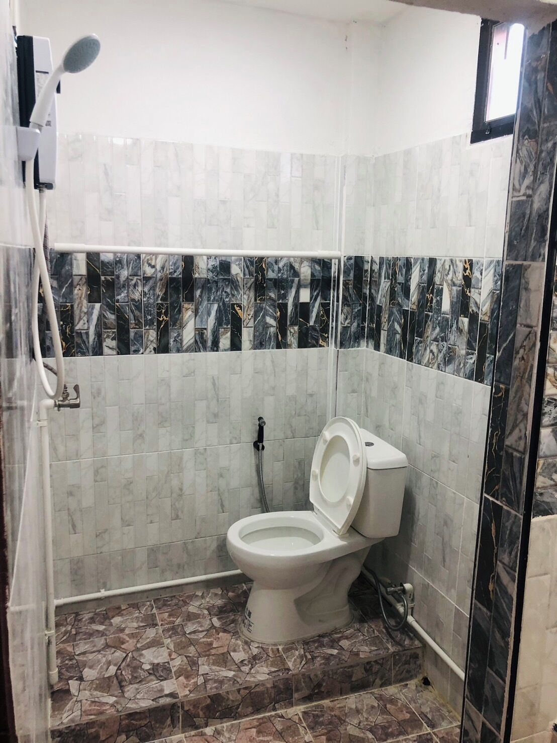 A bathroom with a toilet, a shower, and a tiled floor.