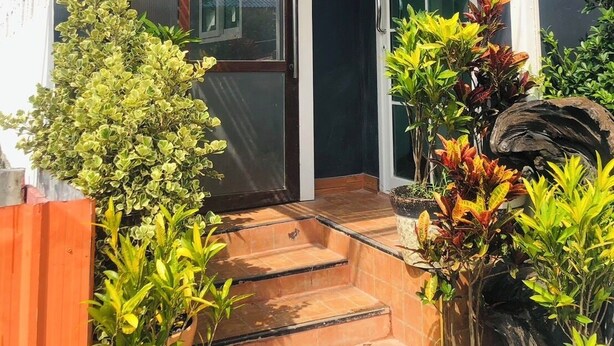 A house entrance with a glass door, a set of steps leading to the door, and various potted plants around the entrance. - SS GUESTHOUSE (Bang Phli)