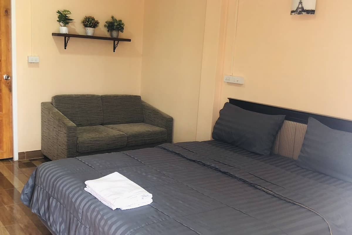 A bedroom with a bed, a grey sofa, and a wall-mounted shelf with plants.