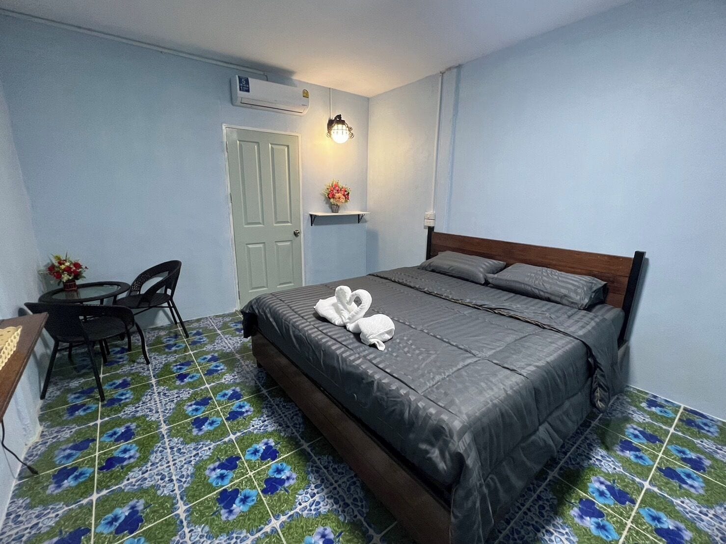 A bedroom with a bed, a desk, a chair, a door, and a wall-mounted air conditioner.