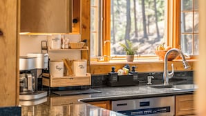 Een moderne keuken met een koffiehoek, een spoelbak en een raam met uitzicht op het bos.