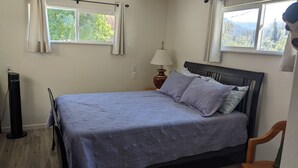 Une chambre à coucher avec un lit, une table de chevet, une lampe, une chaise et une fenêtre avec des rideaux.