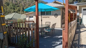 Un espace patio avec une table et des chaises, un parasol bleu et une pancarte sur laquelle on peut lire « Bienvenue ».