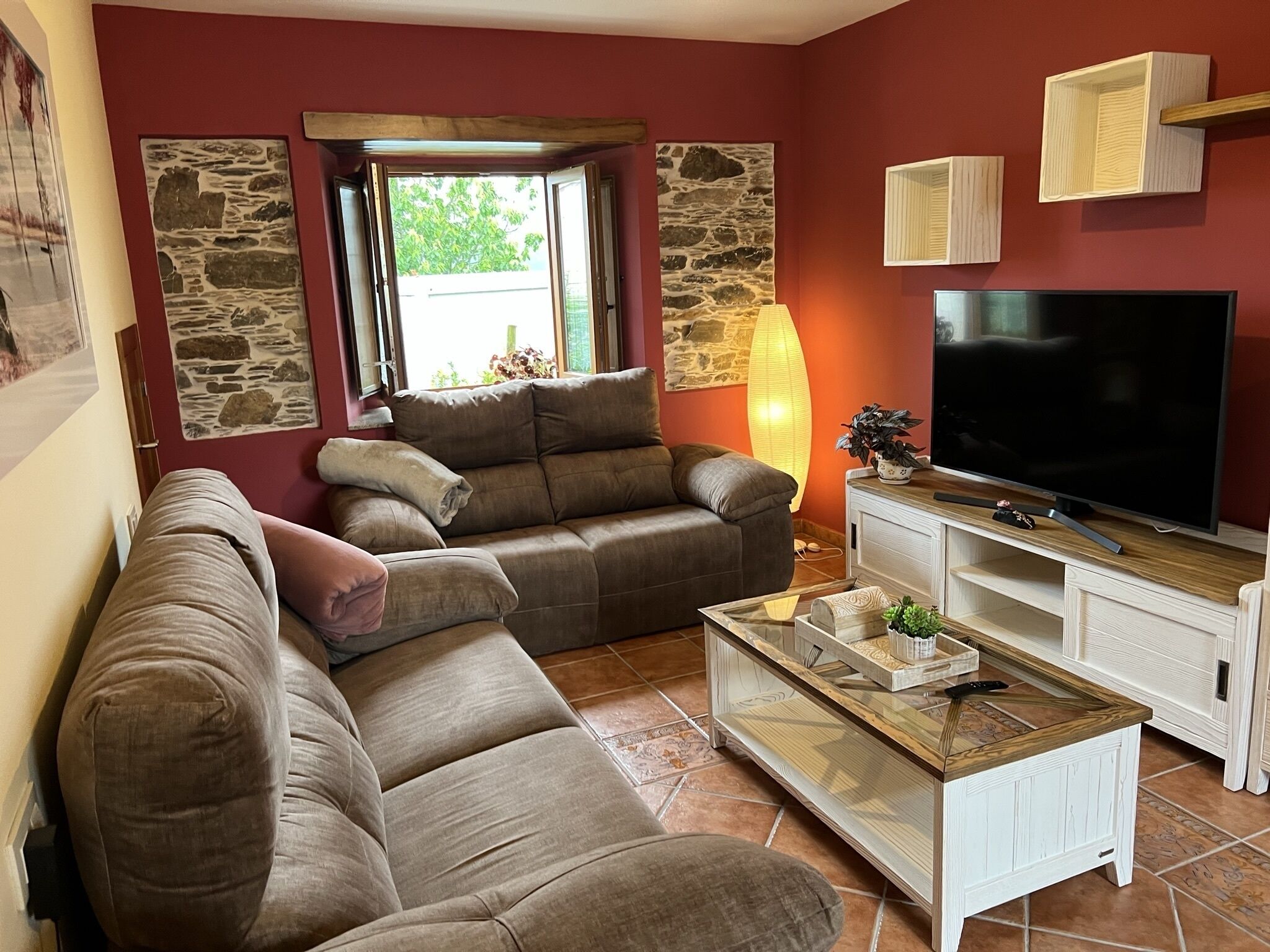 A living room with a brown sectional sofa, a flat-screen TV on a wooden stand, and a stone wall.