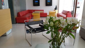 A modern hotel lobby with a red sofa, a glass coffee table, and a vase of flowers. - AW HOTEL LUXOR VERSALLES (Cali)