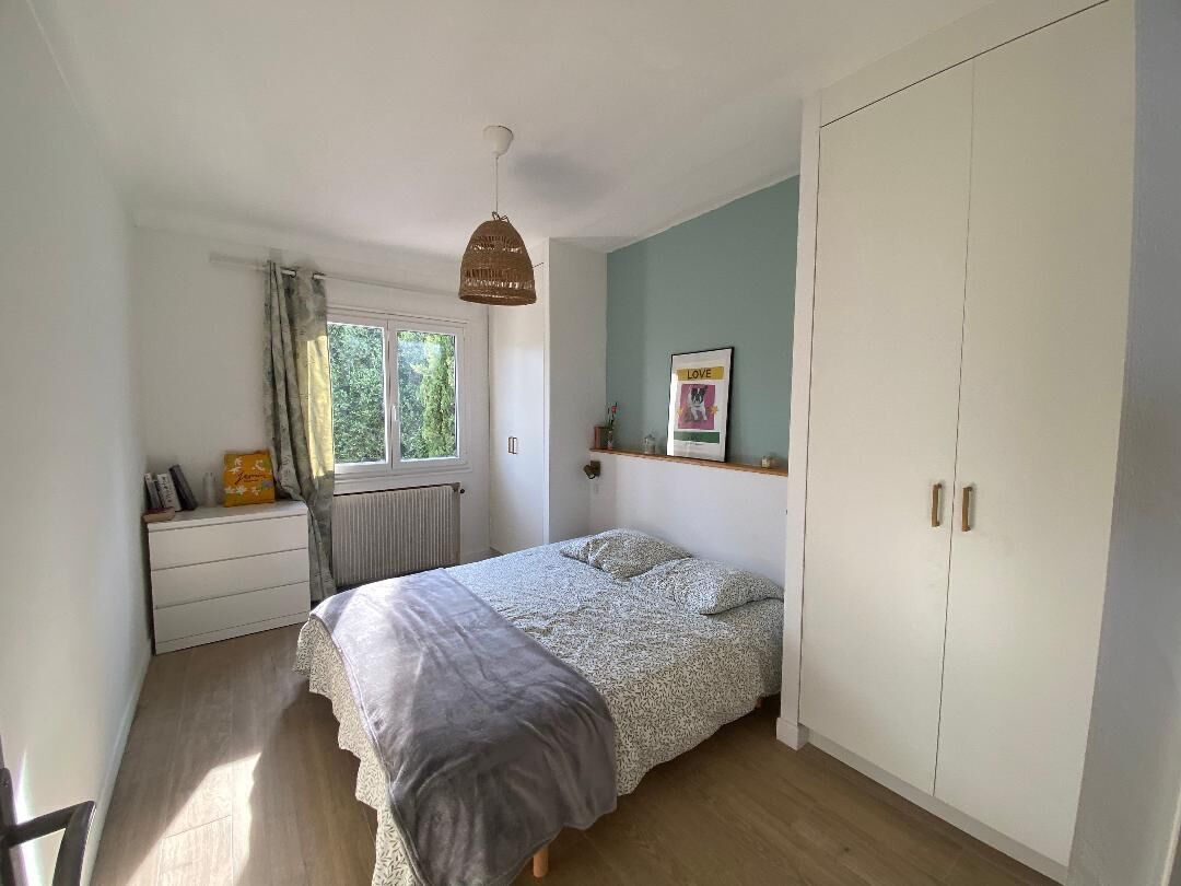 A bedroom with a bed, a window, a radiator, a wardrobe, and a hanging light fixture.