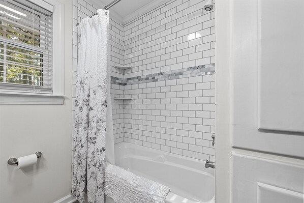 A bathroom with white tiled walls, a shower with a floral curtain, and a bathtub.