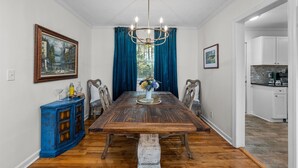 A dining room with a wooden table, blue curtains, a chandelier, and a painting on the wall.