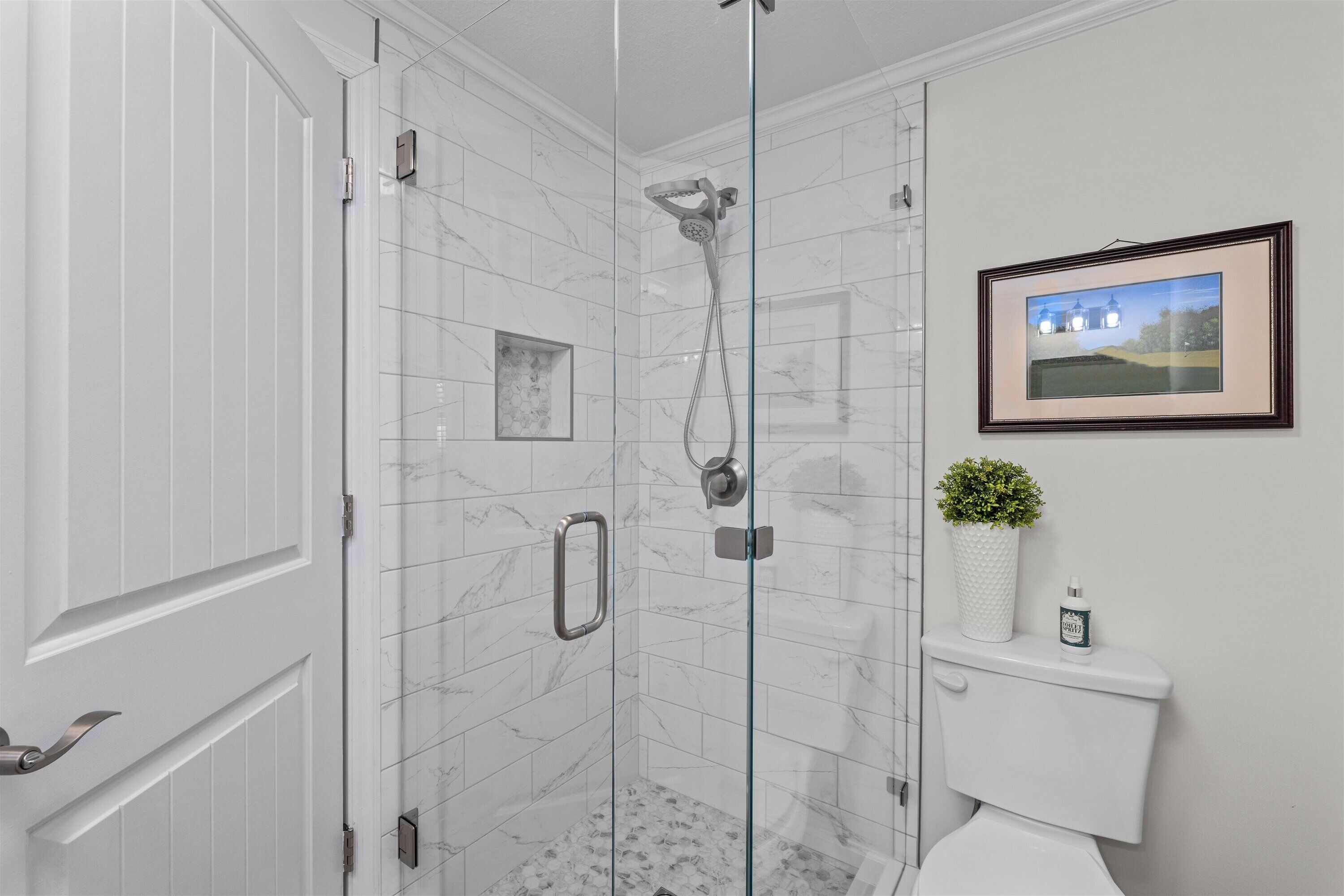 A modern bathroom with a glass-enclosed shower, a toilet, and a framed picture on the wall.