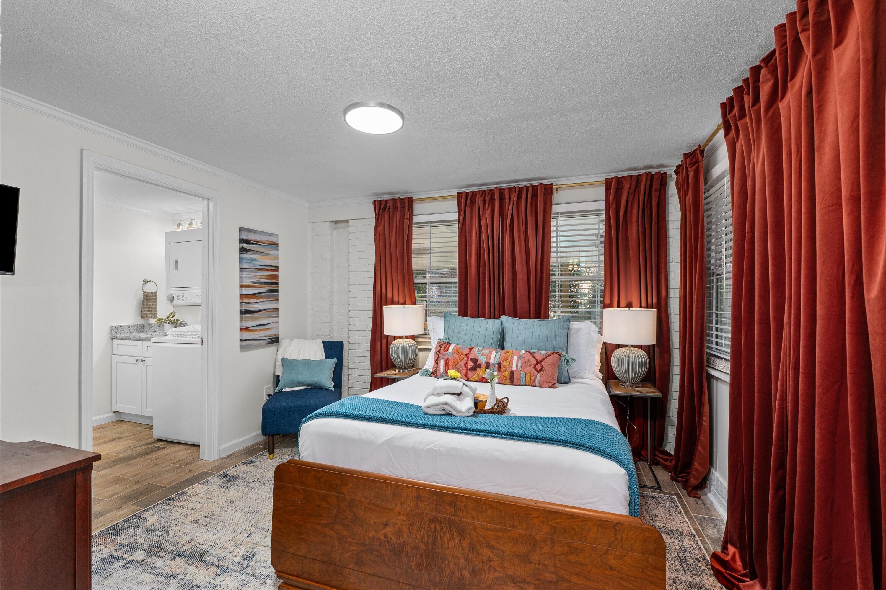 A well-lit bedroom with a large bed, red curtains, and a bedside table with a lamp.