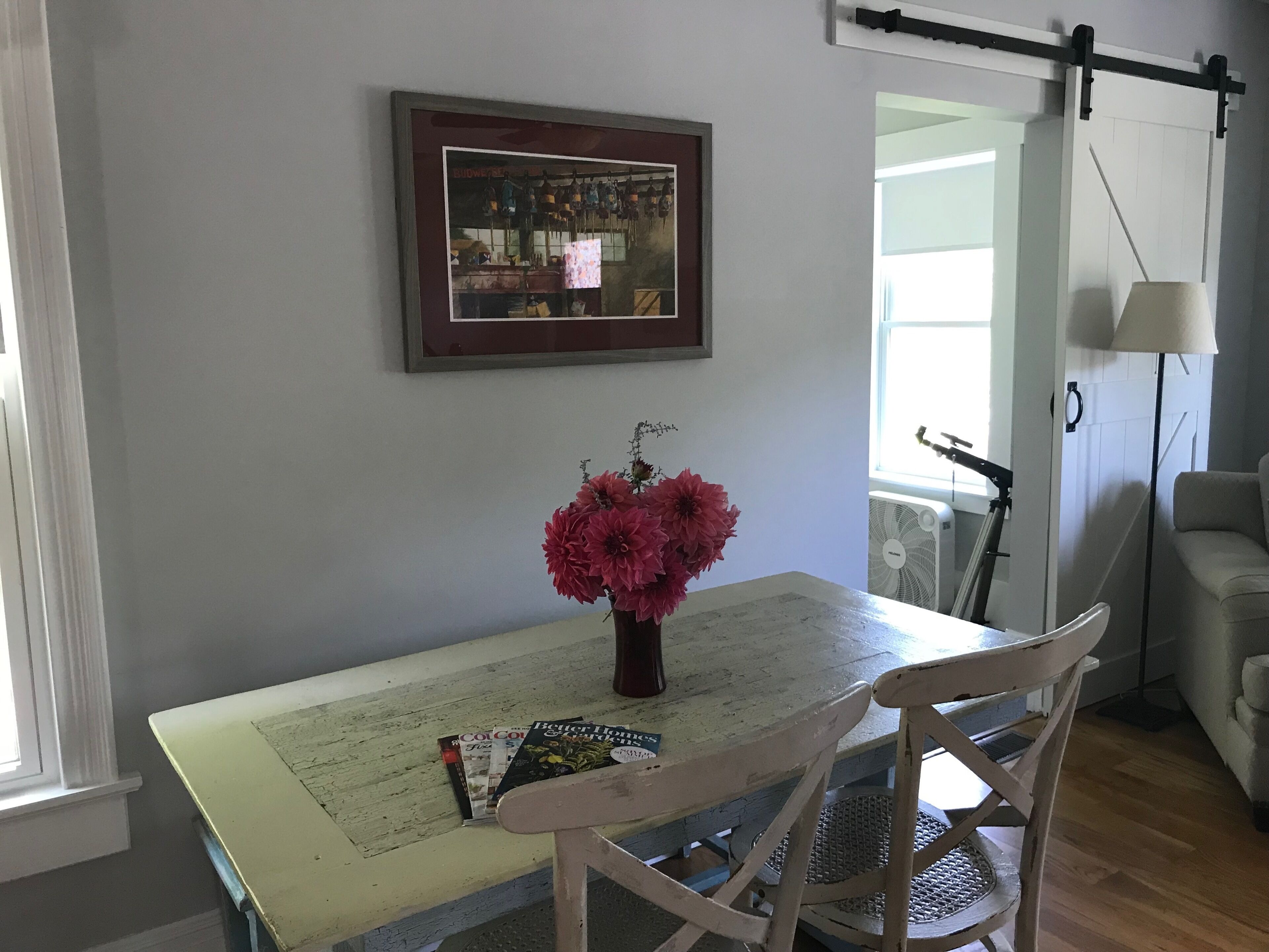 Een eethoek met een tafel, stoelen, een vaas met bloemen, een ingelijste foto aan de muur en een raam met uitzicht.