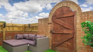 Eine Terrasse mit Ecksofa, Backsteinmauer und hölzernem Tor.