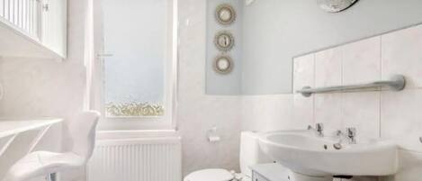 A bathroom with a toilet, a sink, a mirror, and a window.