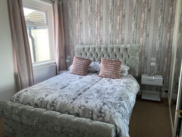 A bedroom with a tufted headboard, a patterned bedspread, and a bedside table with a lamp.